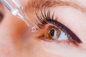A close-up of a person’s eye as a dropper applies liquid, possibly eye drops, just above the eye—showcasing skin and eyelashes. Perfect for illustrating professional eye care Suffolk County residents trust.