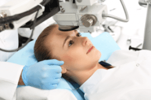 A person lies on a medical bed with their head positioned under a laser eye surgery machine. An Optometrist Suffolk County supports their head with a gloved hand, preparing for or performing an advanced eye care Suffolk County procedure.