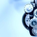 Close-up of an optometry phoropter, an eye examination device with multiple lenses and dials, set against a light blue, blurred background—ideal for showcasing professional eye care in Suffolk County, NY.